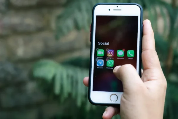Close-up of a hand holding a smartphone displaying social media apps outdoors.