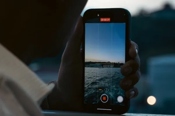 A person records a peaceful waterfront scene using a smartphone at dusk.