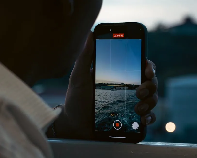A person records a peaceful waterfront scene using a smartphone at dusk.