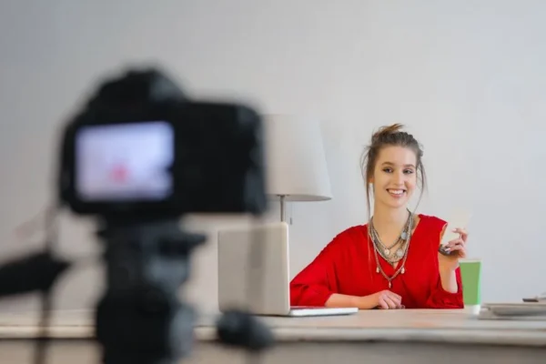 Woman smiling while working on laptop in a modern workspace with digital camera.